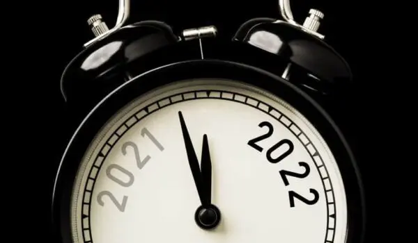 Close-up of an analog alarm clock with "2021" and "2022" on the clock face, showing a few minutes to midnight, against a black background.