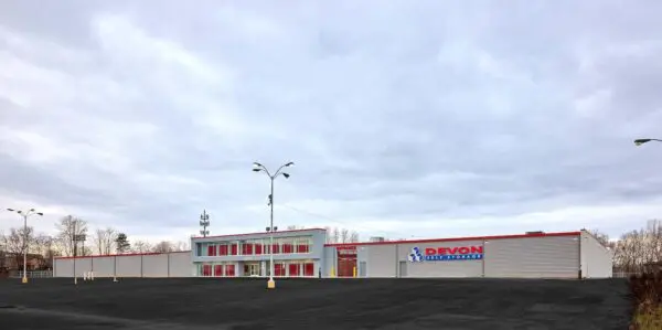 Large, two-story self-storage facility with a red and white exterior, ample parking space, and a cloudy sky in the background.