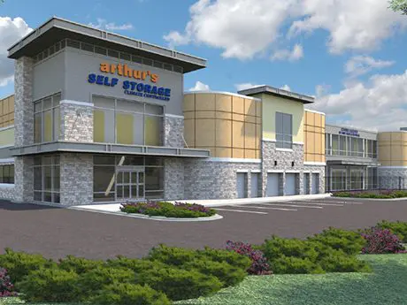 Modern self-storage facility with "arthur's SELF STORAGE" sign on the building, featuring stone and glass architecture, set against a cloudy sky with landscaped surroundings.