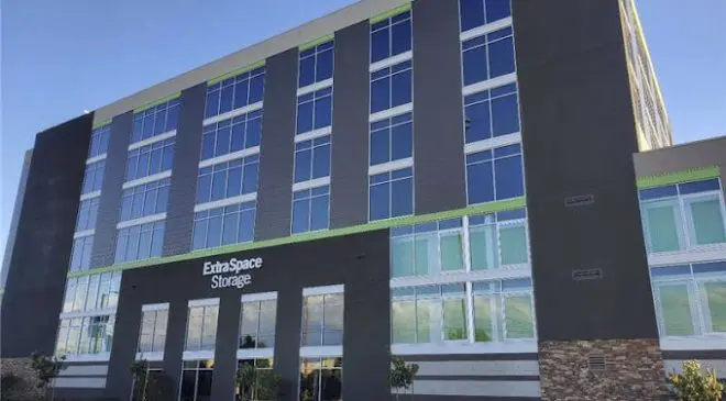 A modern multi-story building with "Extra Space Storage" signage, featuring a combination of glass and dark paneling, set against a clear blue sky.