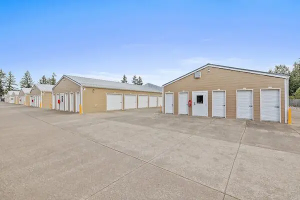 Outdoor view of a storage facility with rows of beige units and white doors, set against a clear blue sky.