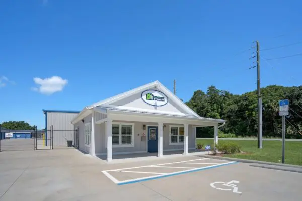 Small building with a white exterior and a sign above the entrance. Handicapped parking space in front and trees in the background under a clear blue sky.