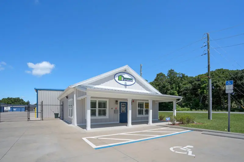 Small building with a white exterior and a sign above the entrance. Handicapped parking space in front and trees in the background under a clear blue sky.