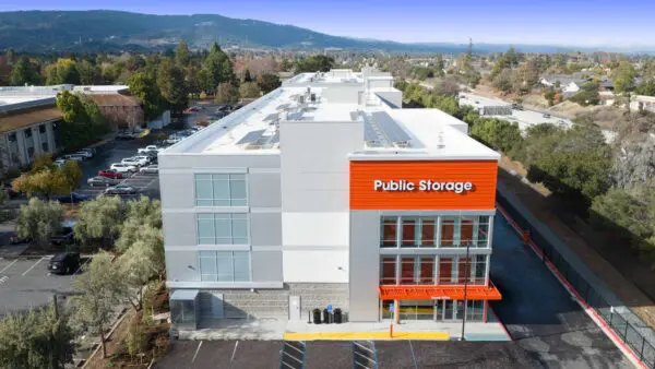 Aerial view of a multi-story Public Storage building with solar panels on the roof, surrounded by a parking lot and green landscape.
