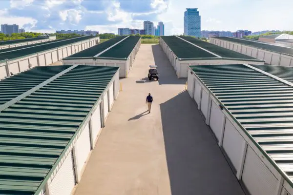 A person walks down the center aisle of a storage facility with green roofs, under a partly cloudy sky, while a golf cart is parked ahead.