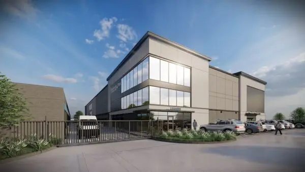 Modern three-story office building with large windows, parking spaces, and a gated entrance. Several cars and a few people are visible under a blue sky with scattered clouds.