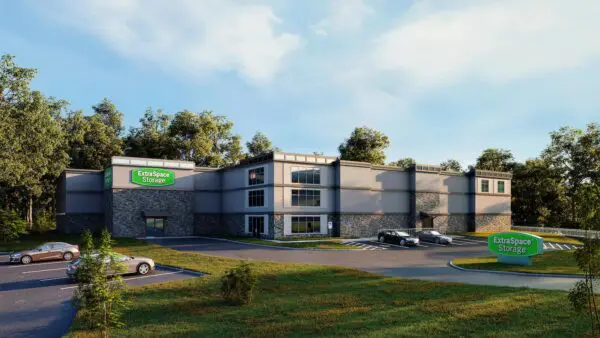 A modern storage facility with several parked cars, surrounded by trees. A green sign reads "Extra Space Storage.