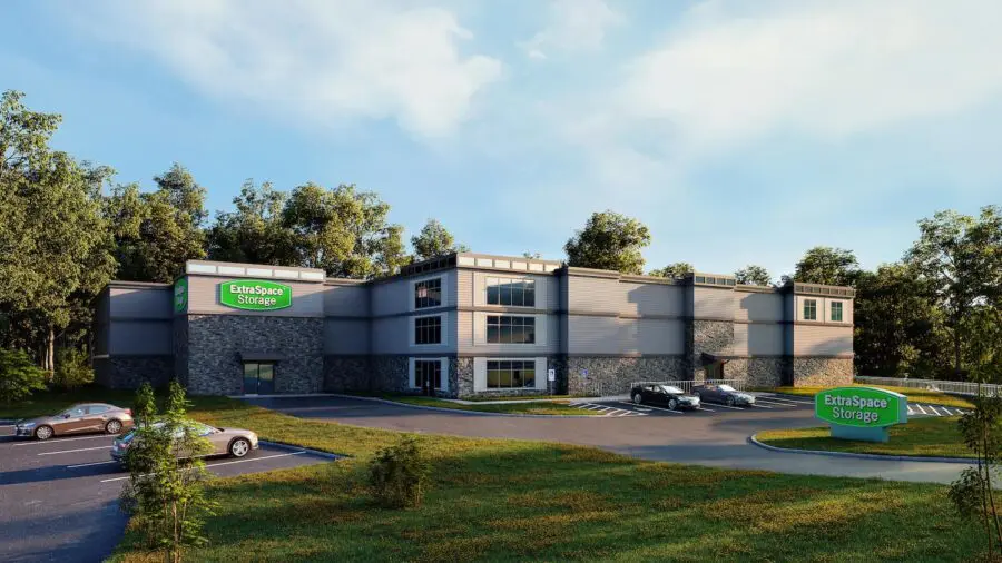 A modern storage facility with several parked cars, surrounded by trees. A green sign reads "Extra Space Storage.