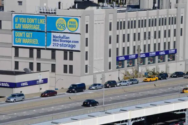 Billboard on a building reads, "If you don't like gay marriage, don't get gay married. Manhattan Mini Storage." Cars drive on the road below.
