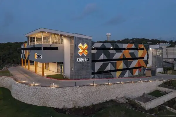 A modern commercial building with a geometric patterned facade and the sign "XSPACE" illuminated at dusk.