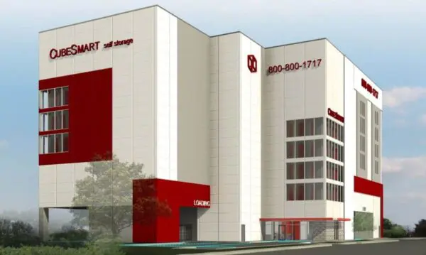Modern multi-story CubeSmart self-storage facility with white and red exterior, displaying company logo and contact number. Surrounded by greenery and a clear sky.