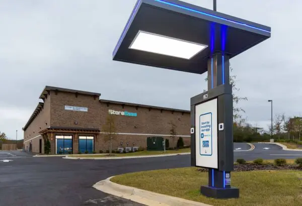 Drive-thru check-in kiosk at a self-storage facility with a brick building in the background and cloudy sky.