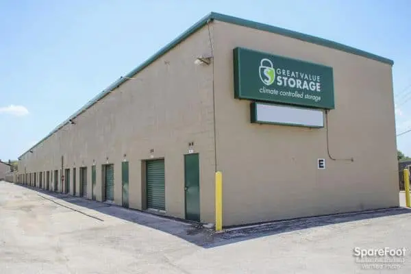 Side view of a beige storage facility with multiple green doors and a sign reading "Great Value Storage, climate-controlled storage" on the side.