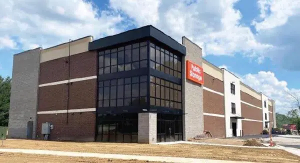 A two-story commercial building with a red "Public Storage" sign, featuring large glass windows and a brick facade, set against a cloudy sky.