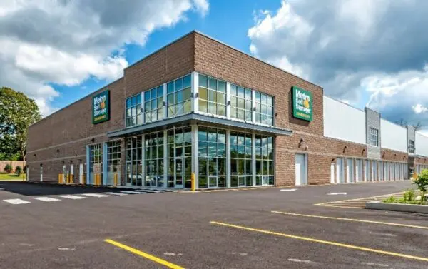 Large storage facility with glass entrance and multiple units, located in a parking lot under a partly cloudy sky.