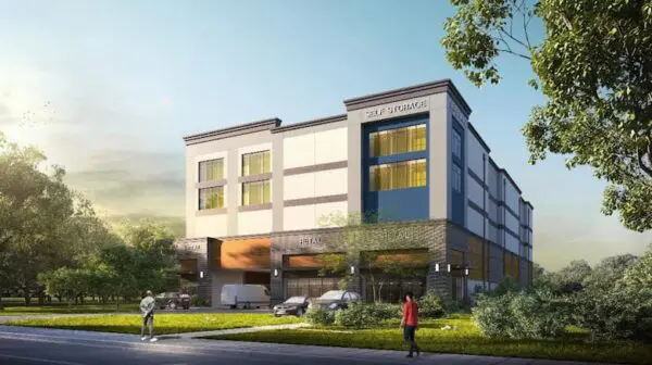 Modern self-storage facility with three stories, large glass windows, and retail space at the ground level, surrounded by greenery and a road with two pedestrians.