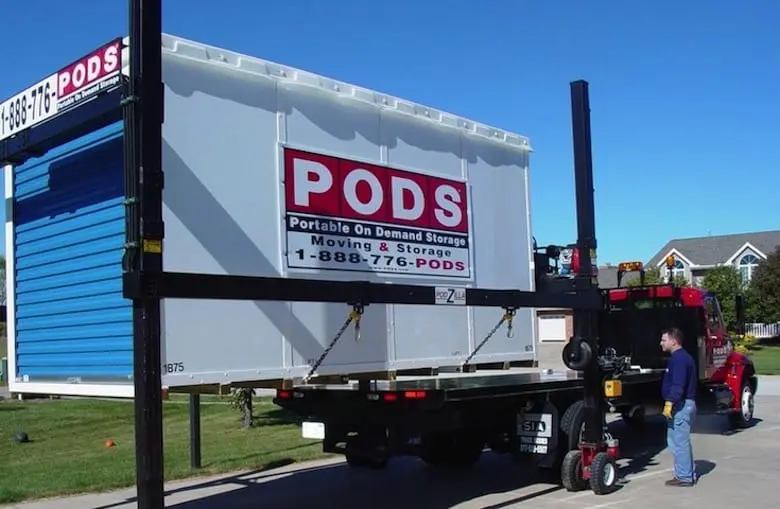 A PODS storage container being loaded onto a truck by a forklift, with a man operating the machinery.