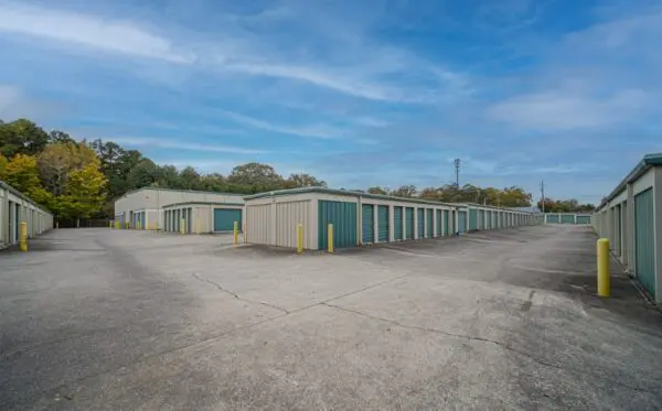 Outdoor self-storage facility with multiple rows of beige and green storage units under a clear blue sky.