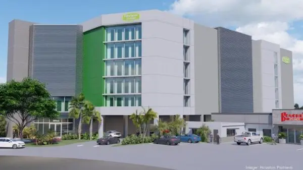 Modern six-story hotel building with green and grey facade, surrounded by palm trees. Several cars are parked in front, adjacent to a smaller building with a red sign.