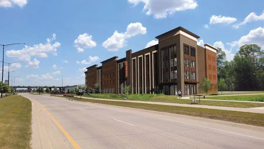 Four-story brick storage building with large windows alongside a wide road, clear sky, and a few trees.