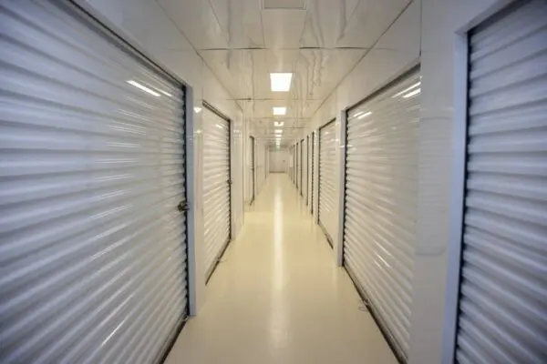 A corridor with white storage unit doors on both sides, bright overhead lighting, and a shiny beige floor.