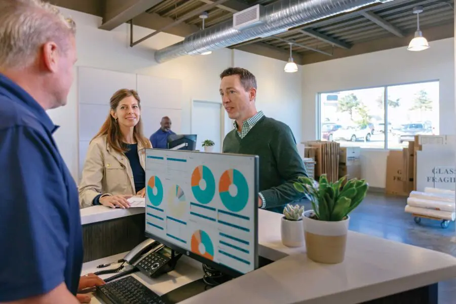 A person at a customer service desk is helping two people on their computer.