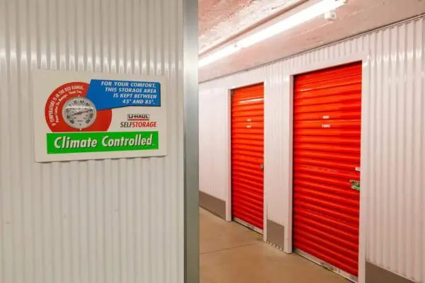 Interior view of a climate-controlled storage facility with corrugated metal walls, labeled doors, and red roll-up doors. A sign indicates the temperature range is between 45°F and 85°F.