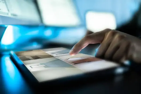 A person using a touchscreen tablet displaying images of interior designs, with a finger poised to select one.