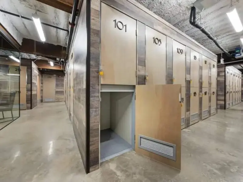 A storage facility hallway with numbered wooden lockers. One locker door, labeled "101," is open, showing an empty interior space.