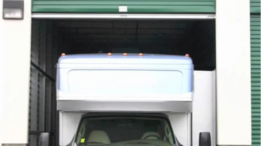 A truck trying to fit into a storage unit with a slightly narrow opening, showing part of the truck cab and closed garage door.