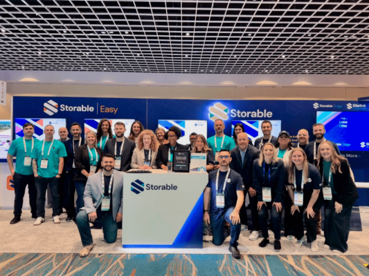 A group of people posing in front of a booth with "Storable" signs at a convention center, under a checkered ceiling.
