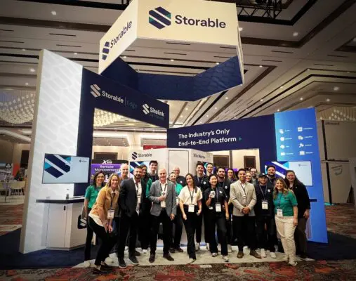 A group of people pose in front of the Storable booth at a convention, with screens and signage displaying the company's branding and platform information.