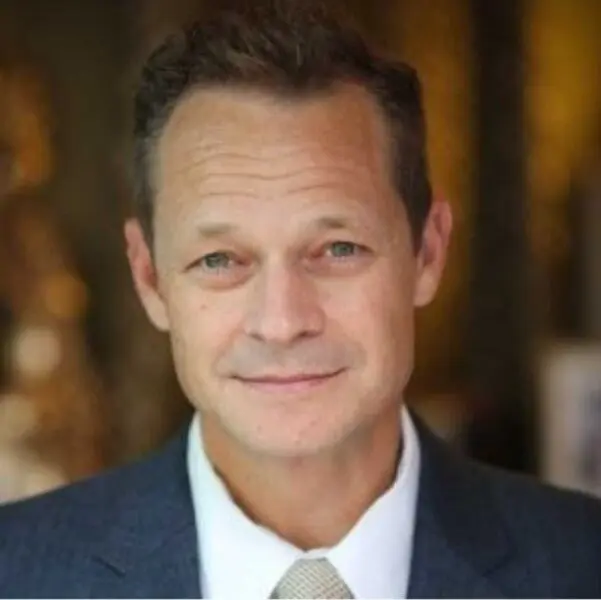 A middle-aged man with short light brown hair wearing a suit and tie, looking at the camera with a neutral expression.