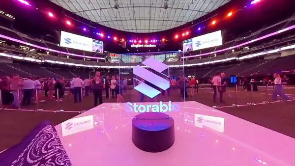 A large group of people gathers inside a stadium near a lit Storable sign; event screens and "allegiant stadium" signage are visible in the background.