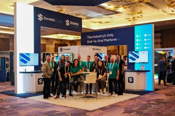 A group of people poses in front of a trade show booth for Storable and SiteLink, featuring branded signage and illuminated displays in a convention center setting.
