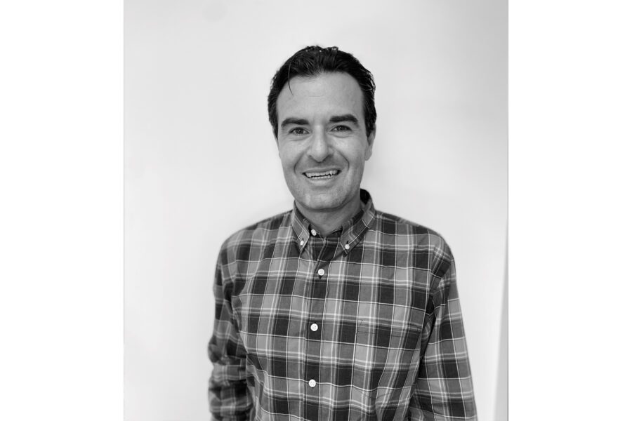 Man in a plaid shirt smiling against a plain background, black and white image.