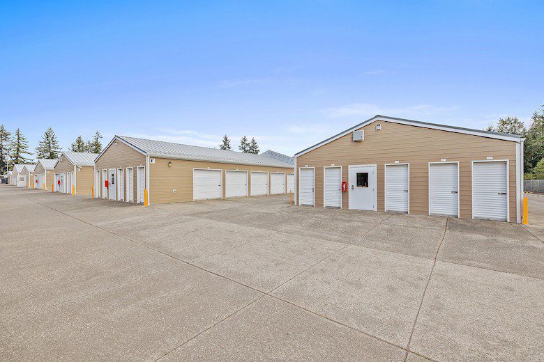 Outdoor view of a storage facility with rows of beige units and white doors, set against a clear blue sky.