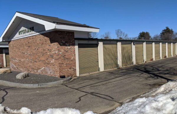 Snow-lined storage facility with multiple closed, brown roll-up doors under a clear blue sky.