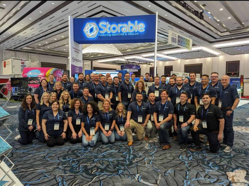 A large group of people in matching uniforms pose for a photo under a sign that reads "Storable" at a convention center.