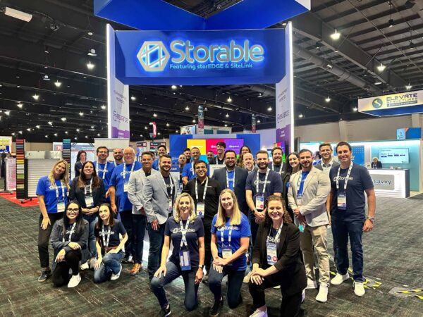 A group of people wearing matching shirts pose for a photo in front of a "Storable" booth at a convention center.