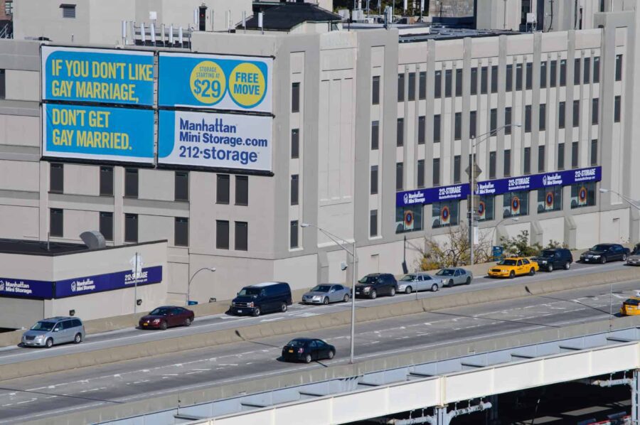 Billboard on a building reads, "If you don't like gay marriage, don't get gay married. Manhattan Mini Storage." Cars drive on the road below.
