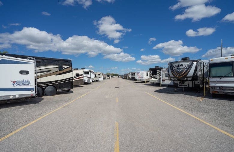A parking lot filled with various recreational vehicles (RVs) under a clear blue sky with scattered clouds.