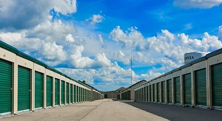 A wide view of a storage facility with rows of green garage doors under a blue sky with clouds.