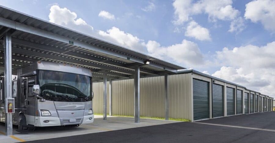 Covered RV parking area with large metal storage units on the right, under a partly cloudy sky.