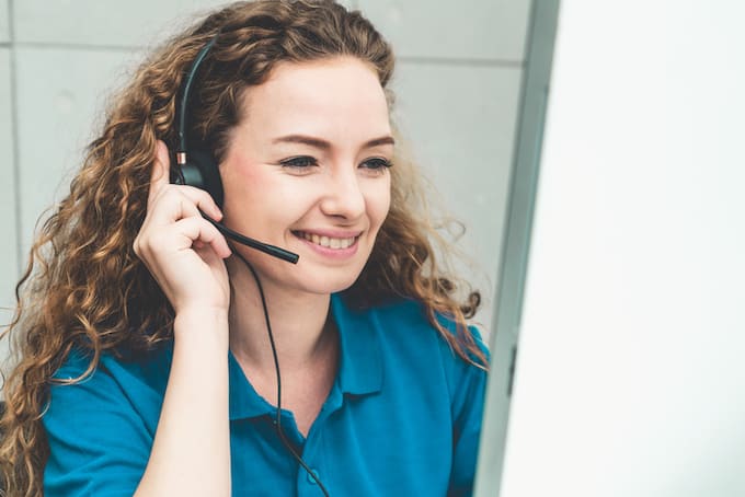 Person with curly hair wearing a headset, smiling while looking at a computer screen.