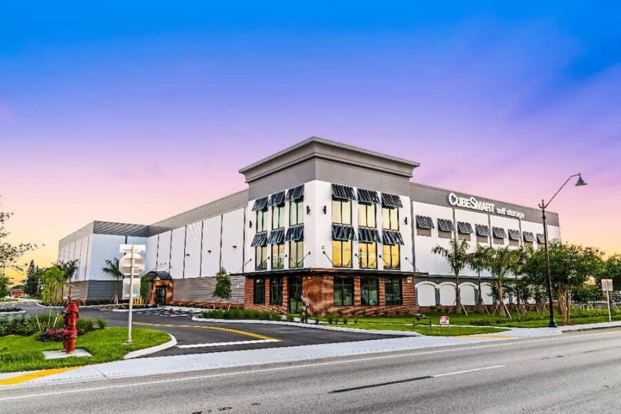 A modern, two-story CubeSmart self-storage building with a mix of glass and brick facade, situated along a suburban street under a clear dusk sky.