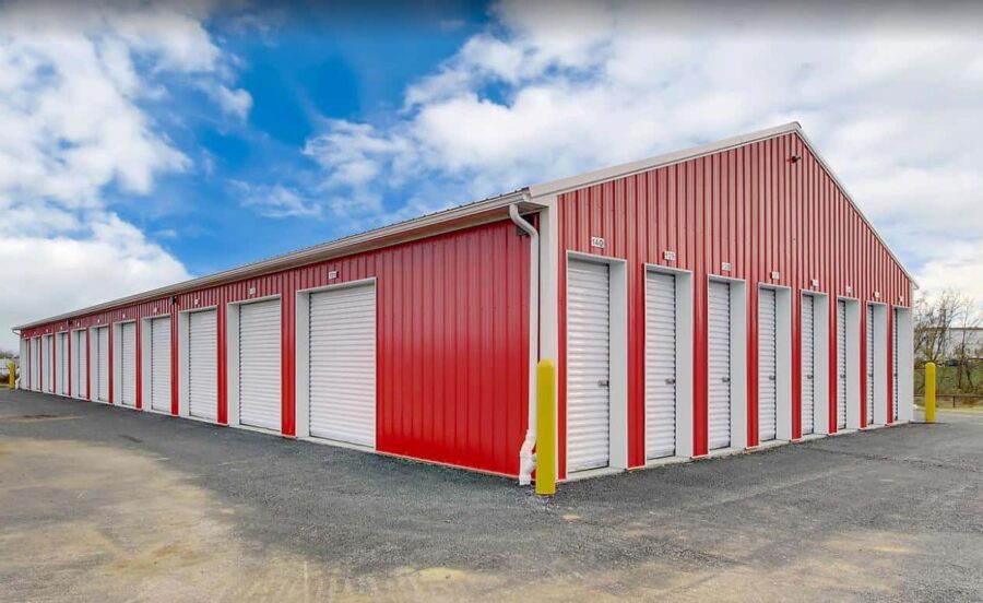 A red metal storage facility with multiple white roll-up doors under a partly cloudy sky.