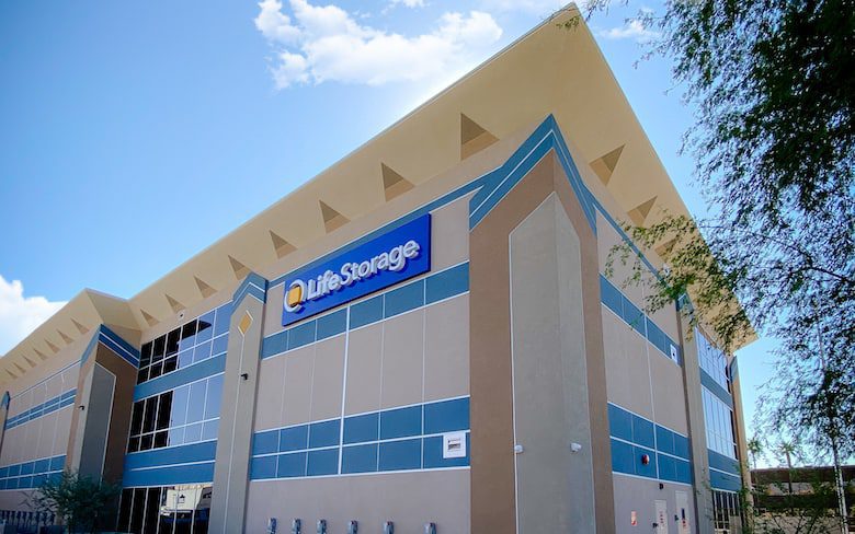 Large building with a "Life Storage" sign, featuring blue and beige exterior accents and a modern design. Sky and trees are visible in the background.