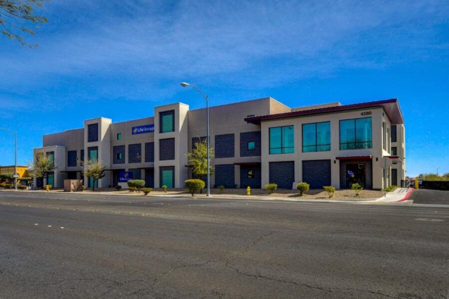 Modern office building with blue accents, large windows, and a flat roof sits along a wide street with clear skies above.