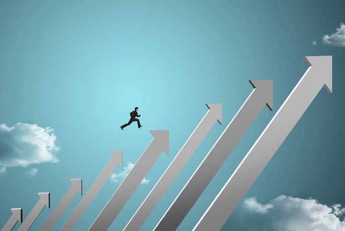 Person in a suit running upwards on a series of ascending arrows against a sky background with clouds, symbolizing progress or growth.